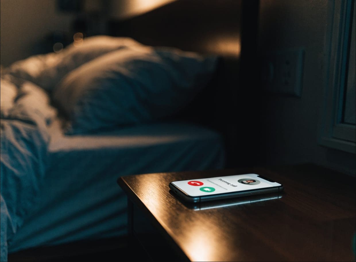 A smartphone glowing on a nightstand showing an incoming call late at night